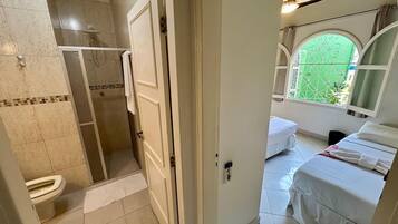A bathroom with a shower, toilet, and a small window.