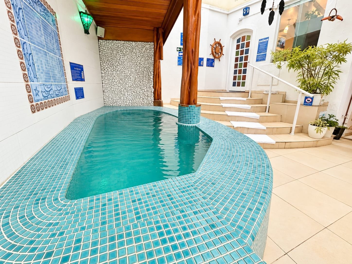 A swimming pool with a tiled edge, a wooden column, and a staircase leading to an upper level.