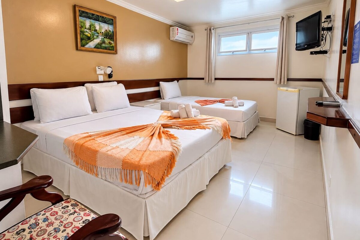 Une chambre d’hôtel avec deux lits, un bureau, une chaise, une télévision et une fenêtre.