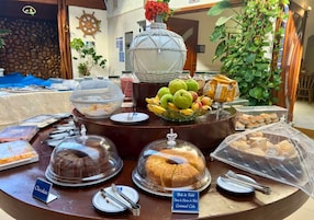 A buffet with various food items, including a chocolate cake, a fruit bowl, and a covered cake stand.