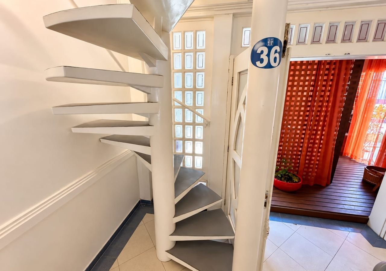 A spiral staircase with a white exterior and a blue sign indicating room number 36.