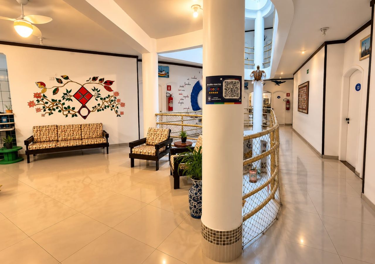 A hotel lobby with a sofa, chairs, a decorative wall, a staircase, and a QR code on a pillar.