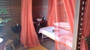 A room with a wooden floor, a bed with a white sheet, a small table, a sink, and a plant. - Hotel Casa Branca (Guarujá)