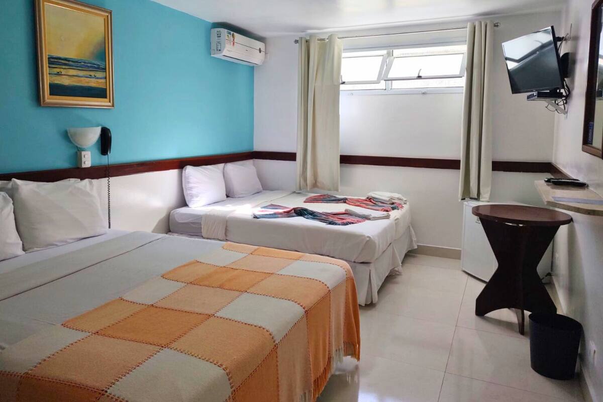 Une chambre d’hôtel avec deux lits, une télévision, un bureau et une fenêtre avec des rideaux.