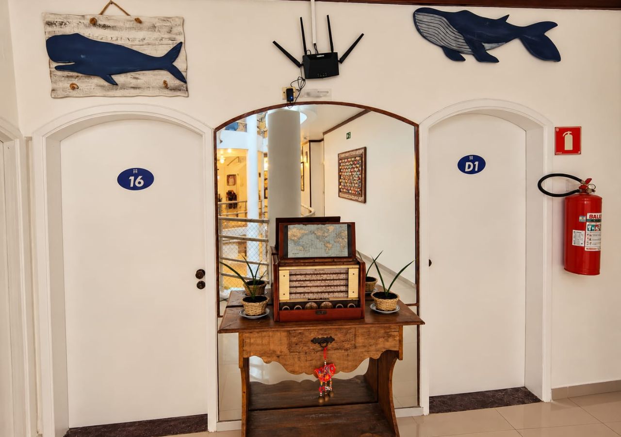 A hallway with two doors, one marked with the number 16 and the other with D1. A wooden console table with a radio and potted plants is in the center.