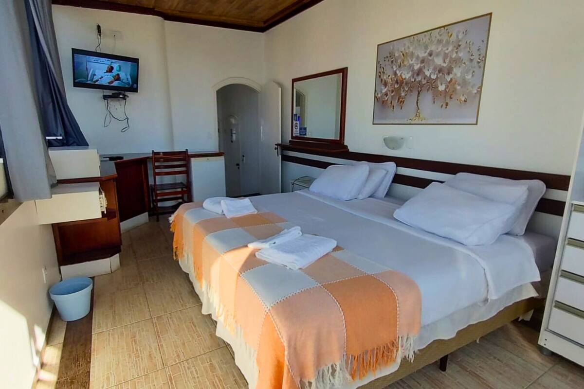 Une chambre d’hôtel avec un grand lit, un bureau, une chaise, une télévision, une porte et un tableau au mur.