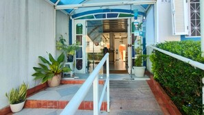 A hotel entrance with a covered walkway, potted plants, and a reception desk. - Hotel Casa Branca (Guarujá)
