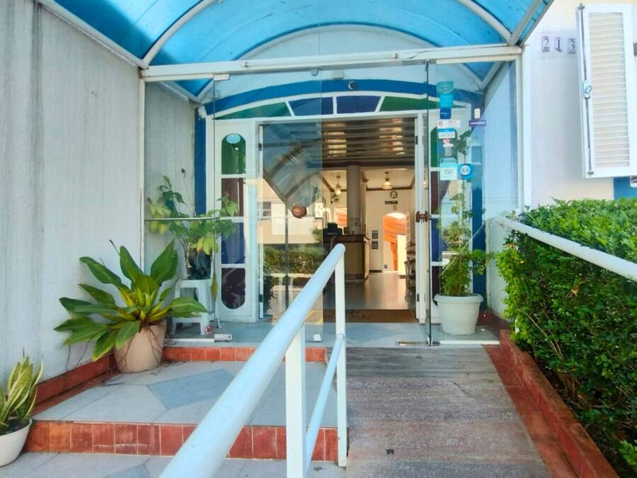 L’entrée d’un hôtel, avec un passage couvert, des plantes en pot et un comptoir d’accueil.