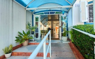 A hotel entrance with a covered walkway, potted plants, and a reception desk.