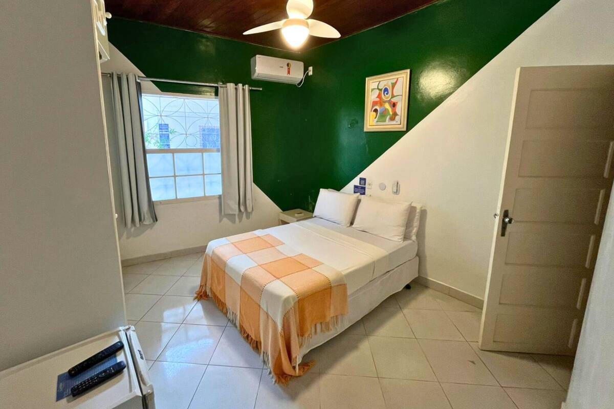 Une chambre à coucher avec un lit, une fenêtre avec des rideaux, un ventilateur de plafond et une porte.