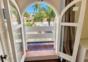 An open doorway leading to a balcony with a view of palm trees and a residential area.
