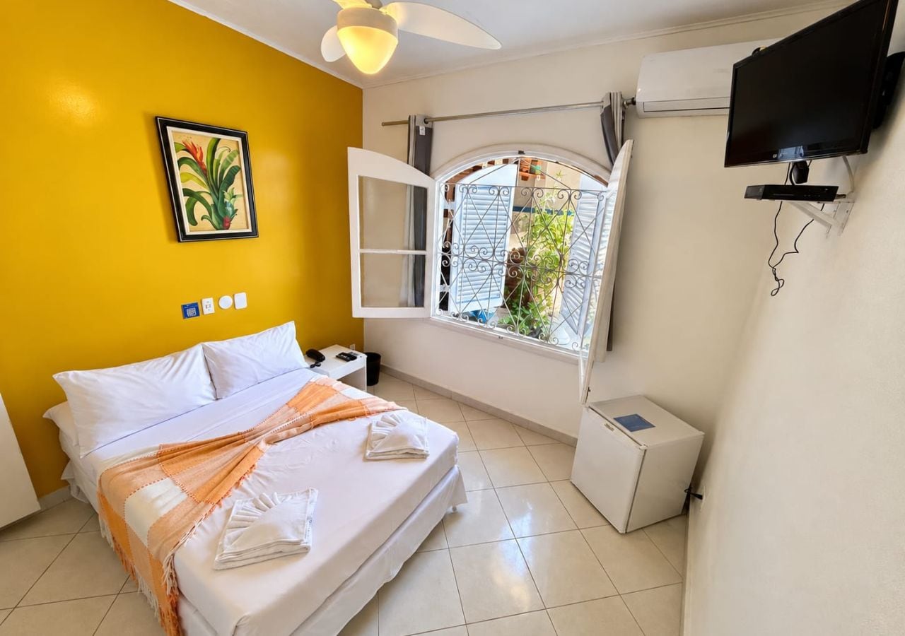 A hotel room with a bed, a window with a view, a TV, and a small white cabinet.