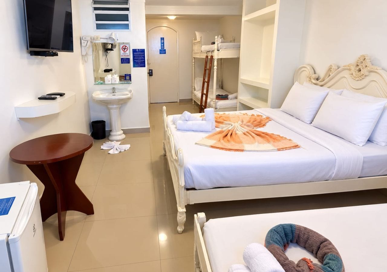 Quarto de hotel com cama, mesa de cabeceira, mesinha redonda, pia e televisão.