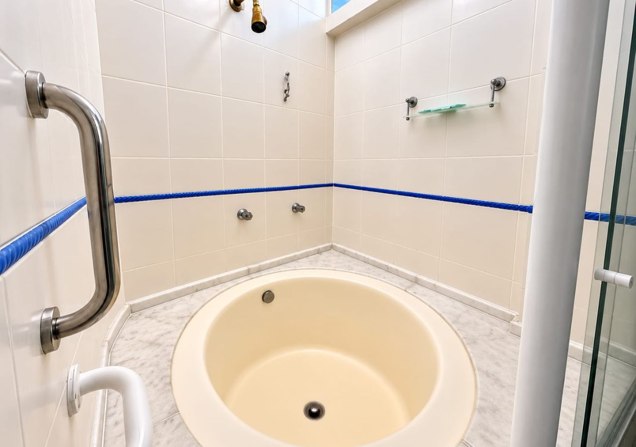 Un baño con bañera, barra de apoyo y mampara de vidrio.