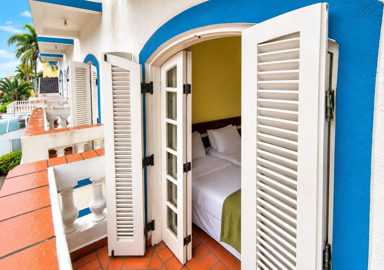 A hotel room with a bed, a balcony, and a view of palm trees.