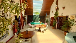 Un patio iluminado por el sol con piscina, sillas blancas y plantas en macetas.