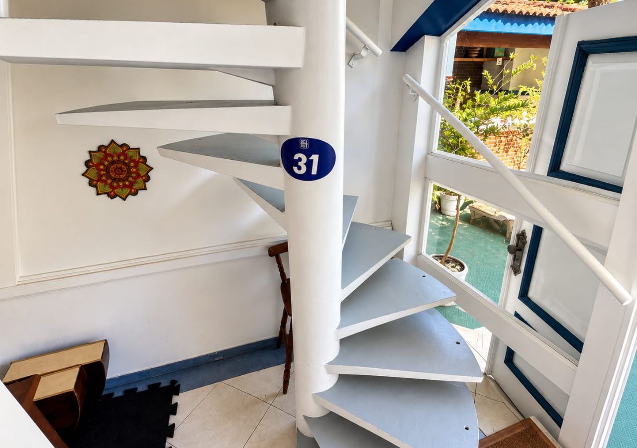 Un escalier en colimaçon orné d’une plaque portant le numéro 31, un élément décoratif mural et une vue sur la verdure à l’extérieur.