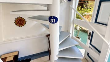 Un escalier en colimaçon orné d’une plaque portant le numéro 31, un élément décoratif mural et une vue sur la verdure à l’extérieur.
