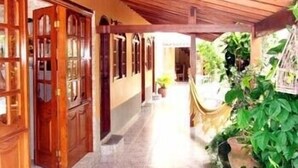 A corridor with wooden doors and windows, leading to a covered outdoor area with plants. - Pousada da Lenna (Rio das Ostras)