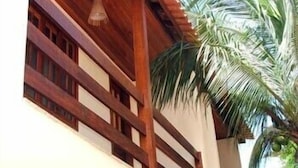 A building with a wooden balcony and a palm tree. - Pousada da Lenna (Rio das Ostras)