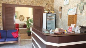 A reception area with a counter, a refrigerator, a couch, and a wall with framed pictures. - Pousada da Lenna (Rio das Ostras)