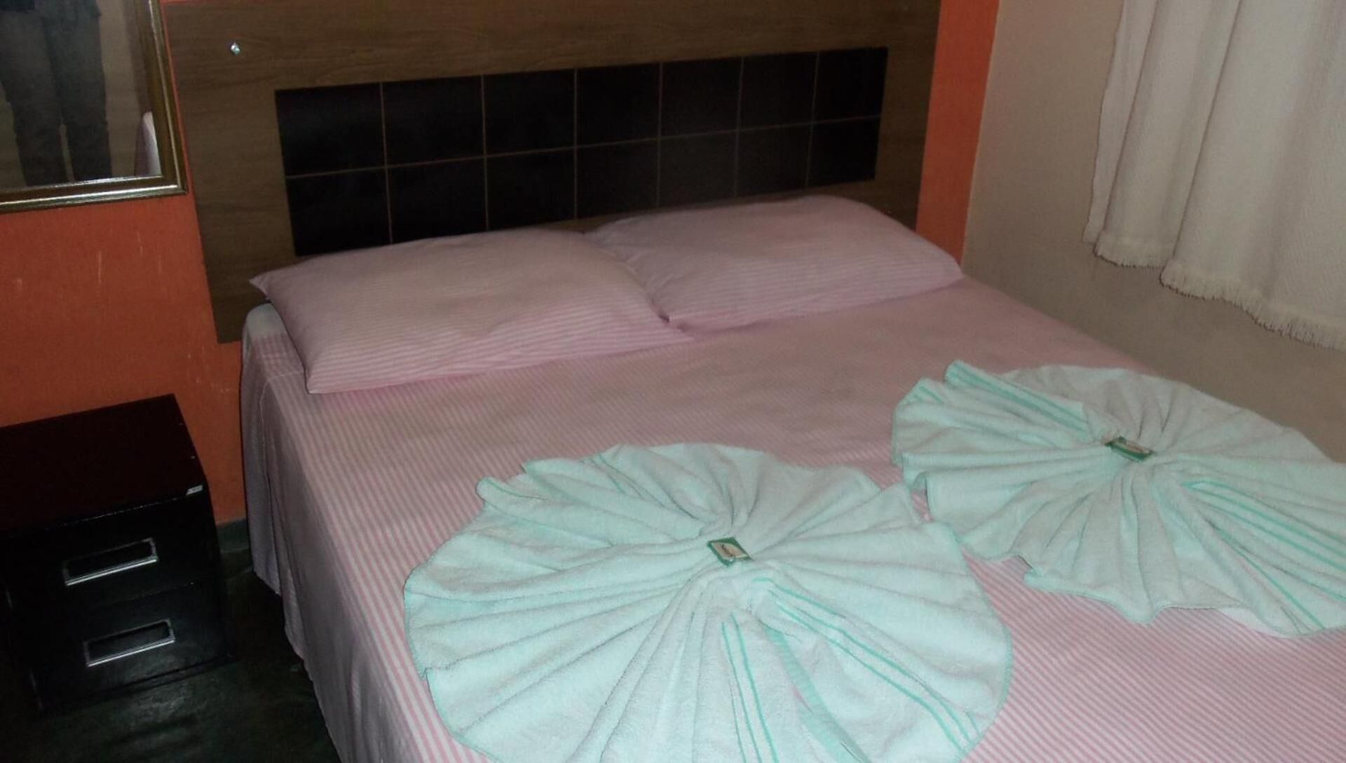 A hotel room with a bed, two pillows, and two folded towels on the bed.