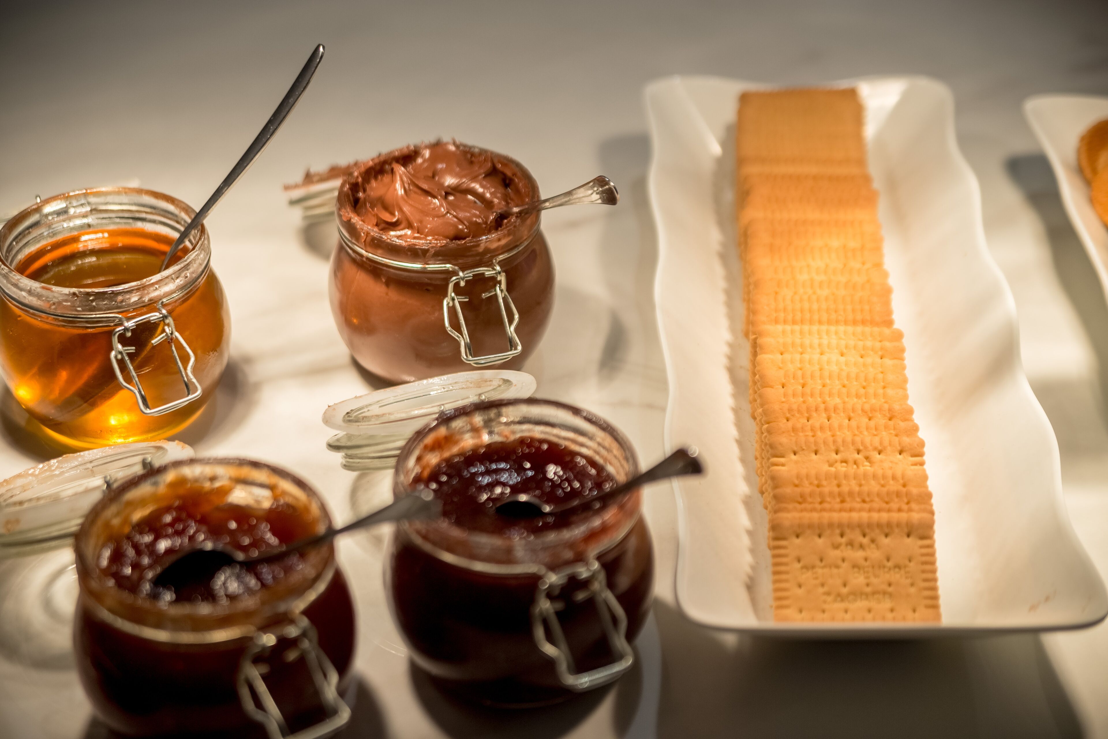 A table with jars of honey and chocolate spread, a loaf of bread, and a plate of crackers.