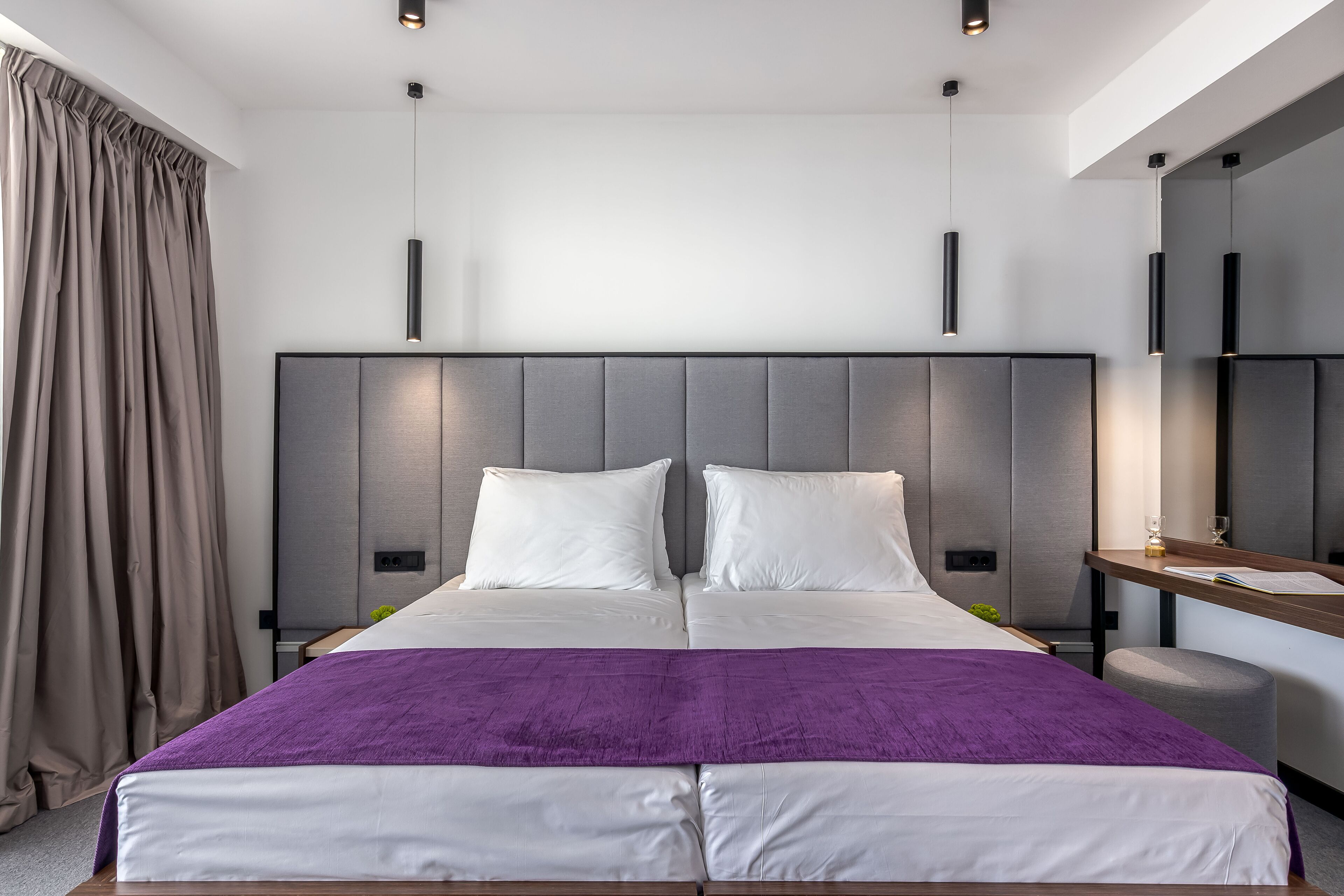 A modern hotel room with a large bed, a bedside table, a nightstand, and a mirror.