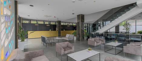 A modern lobby with a staircase, seating areas, and a glass railing.