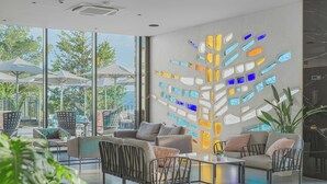 A modern lounge area with comfortable seating, a large glass wall with colorful geometric patterns, and a view of the outdoors. - Hotel Ad Turres (Crikvenica)