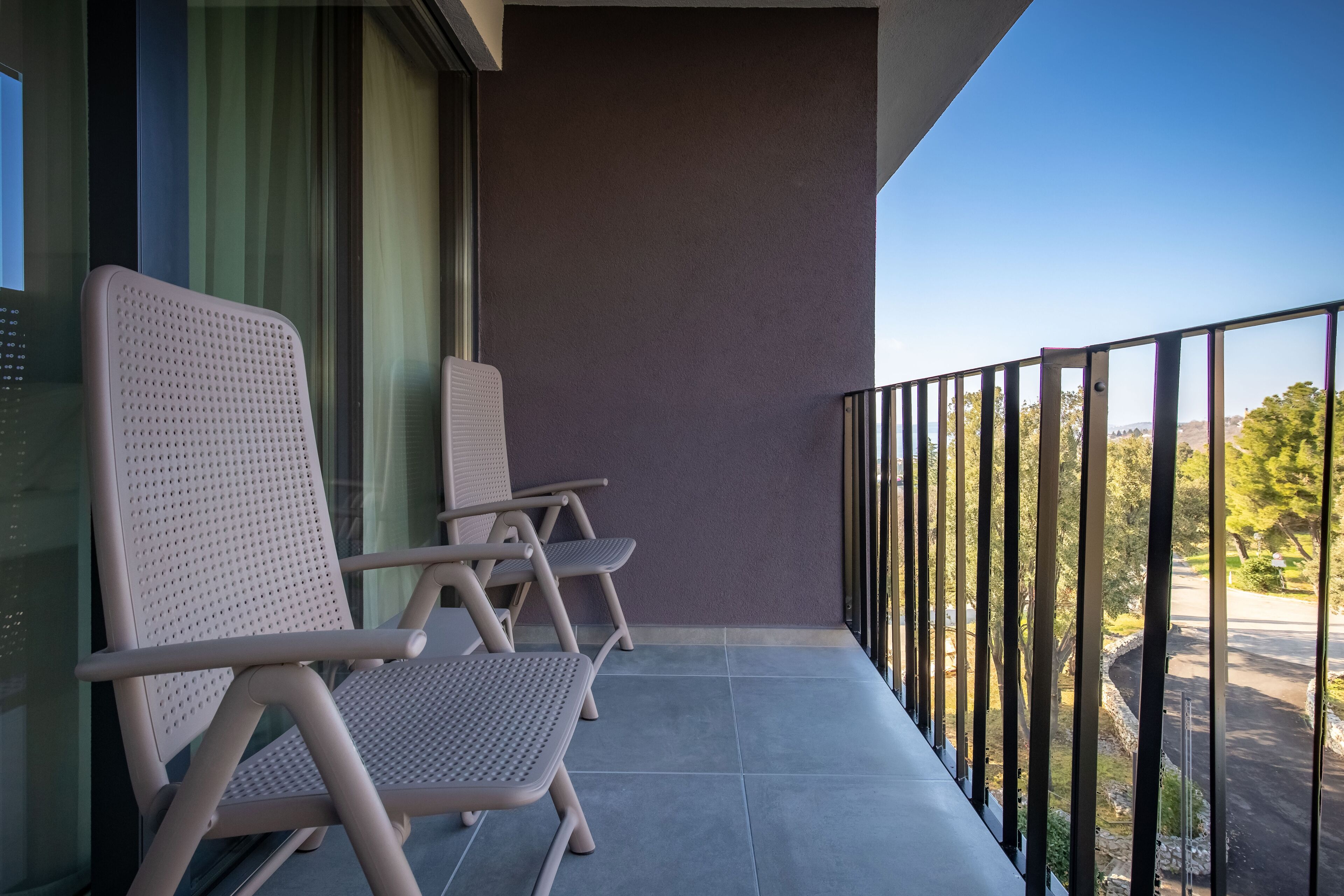 A balcony with two chairs and a table, a view of the street, and a purple wall.