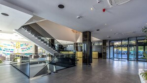 A modern lobby with a glass staircase, a reception desk, and large windows offering views of the outside. - Hotel Ad Turres (Crikvenica)