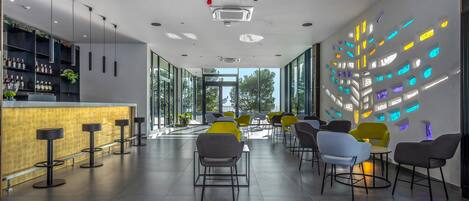 Zona de bar moderna con una barra larga, taburetes y un área de estar con sillas.