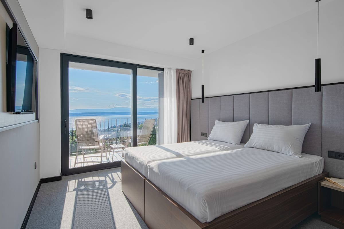 A modern bedroom with a large bed, a TV, and a balcony with a view.