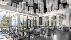 A modern dining area with tables and chairs, large windows, and hanging light fixtures. - Hotel Ad Turres (Crikvenica)