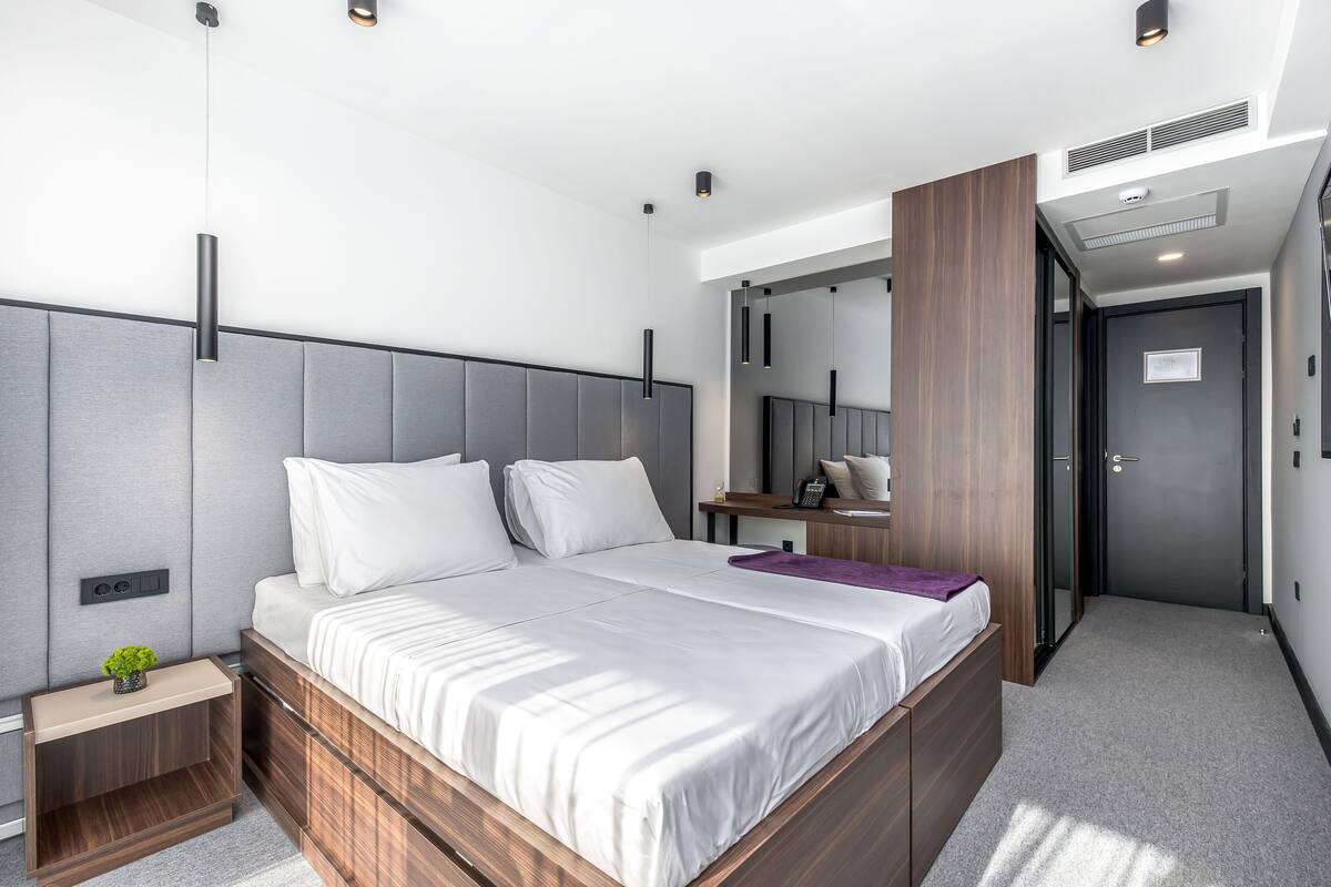 A modern bedroom with a large bed, bedside tables, a mirror, and a walk-in closet.
