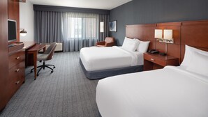 A hotel room with two beds, a desk, a chair, a TV, and a window with curtains.