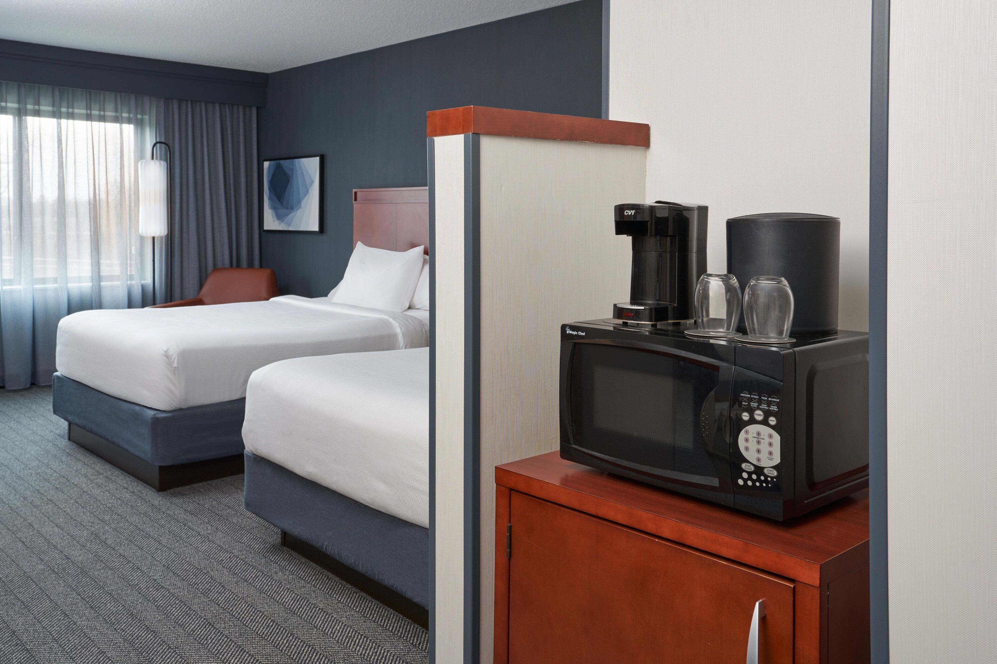 Habitación de hotel con dos camas, un minibar y cafetera.