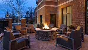 An outdoor patio with a stone fire pit surrounded by wicker chairs and tables.
