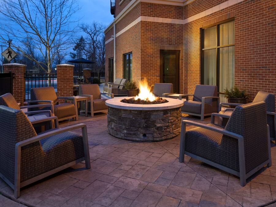 An outdoor patio with a stone fire pit surrounded by wicker chairs and tables.
