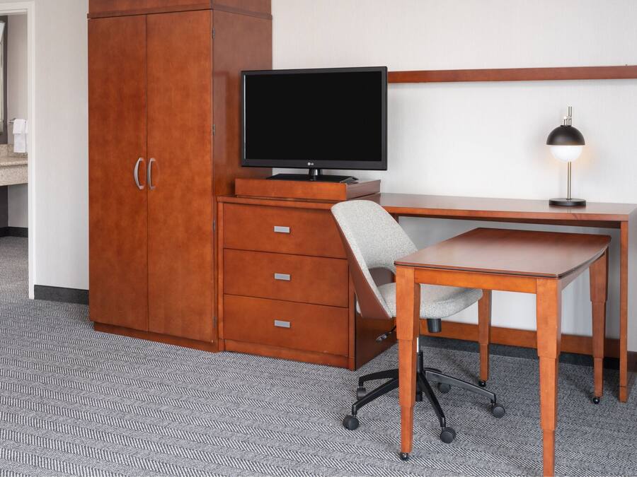 A hotel room with a wooden desk, a television, a chair, and a cabinet.