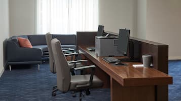Un espacio de oficina moderno con un escritorio de madera alargado, varias sillas, una impresora y un sofá con cojines.