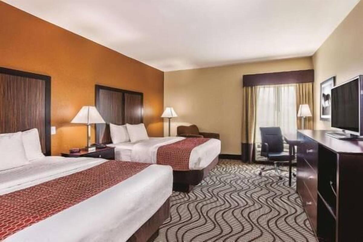 A hotel room with two beds, a desk, a chair, a television, and a window with curtains.
