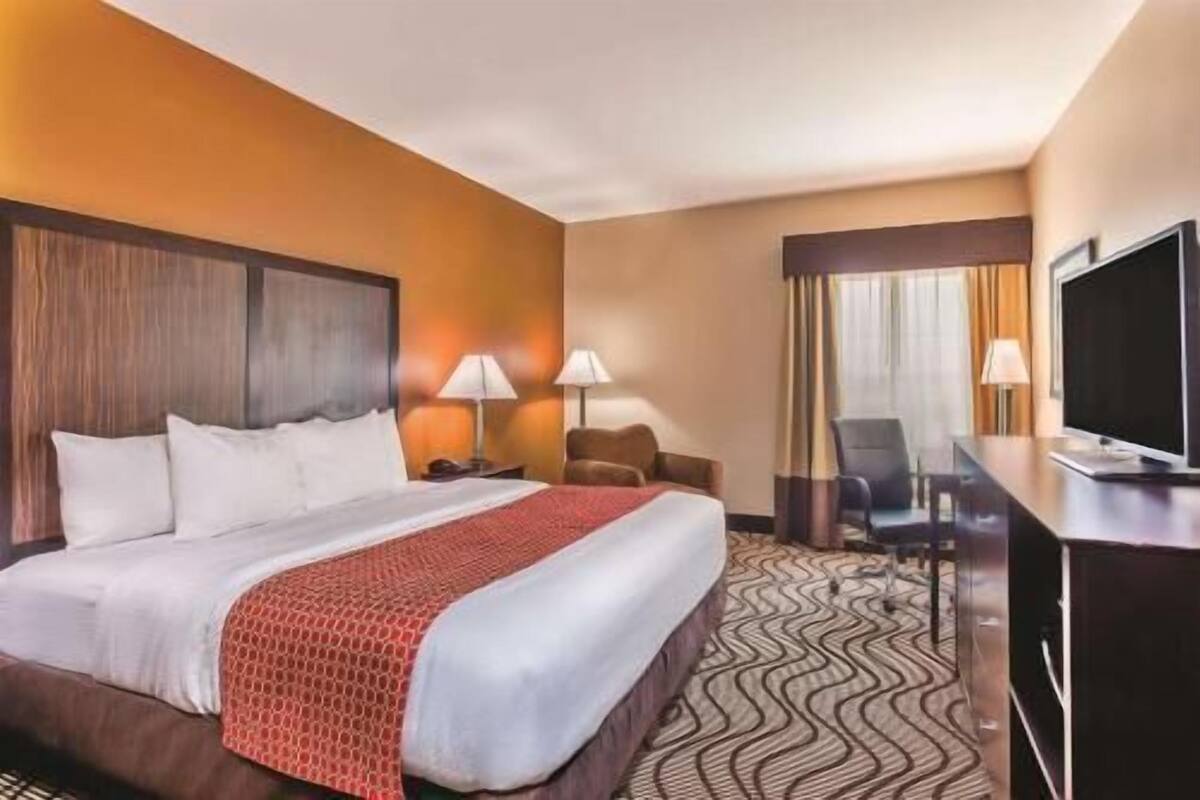 A hotel room with a large bed, two bedside tables with lamps, a desk with a chair, and a television.