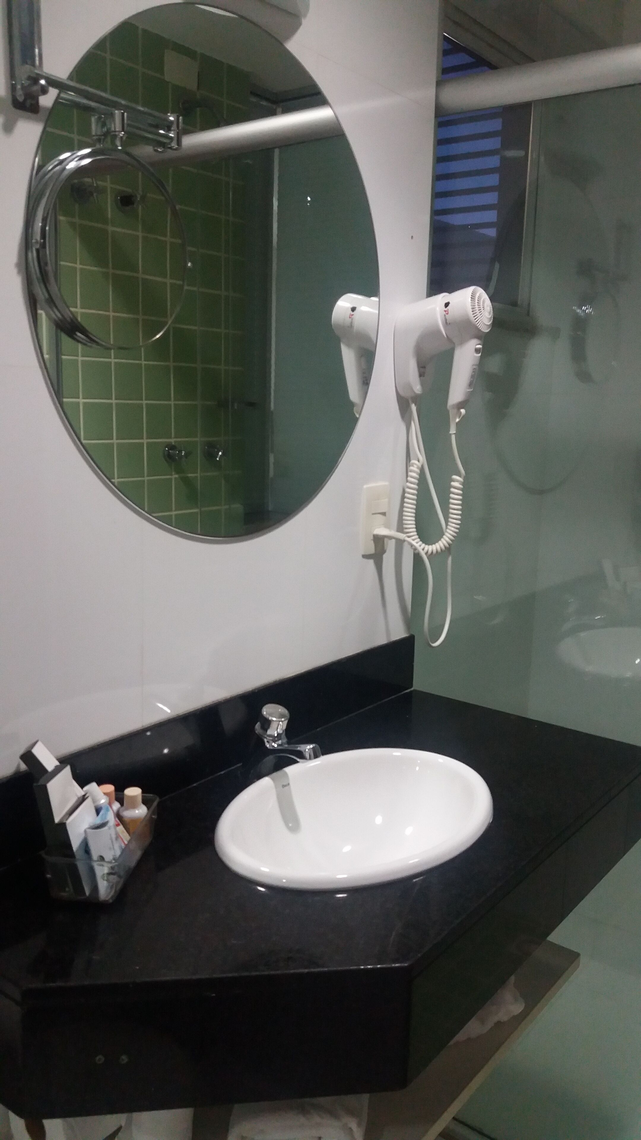 A bathroom with a round mirror, a white sink, and a handheld hair dryer mounted on the wall.