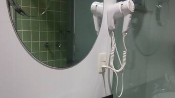 Un baño con un espejo redondo, un lavamanos blanco y un secador de pelo de mano fijado a la pared.