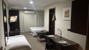 Habitación de hotel con cama, escritorio con silla, televisor, equipo de aire acondicionado y un cuadro en la pared.