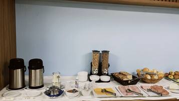 Un buffet de petit-déjeuner comprenant des machines à café, des céréales, du pain et divers autres aliments pour le petit-déjeuner.