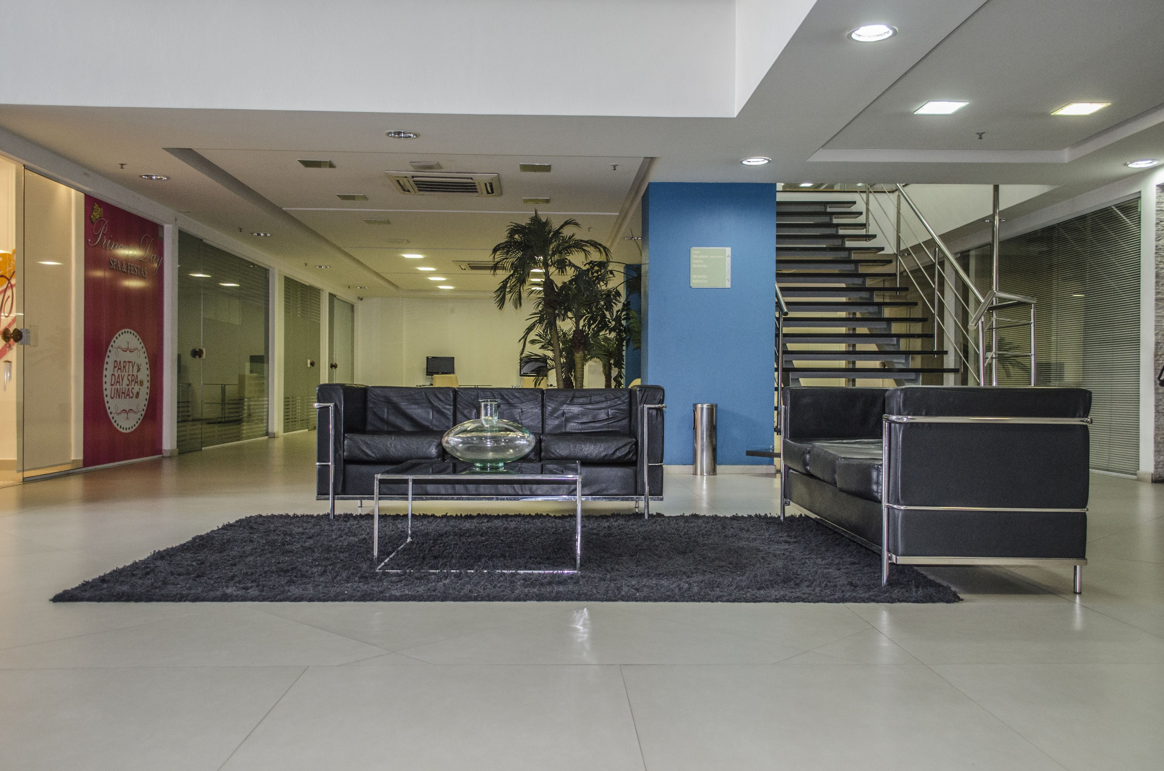A modern lobby with a black leather sofa, a glass coffee table, and a staircase.
