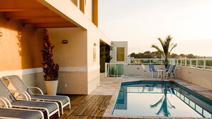 Un área de piscina en la azotea con sillones, una piscina pequeña y una planta en maceta.